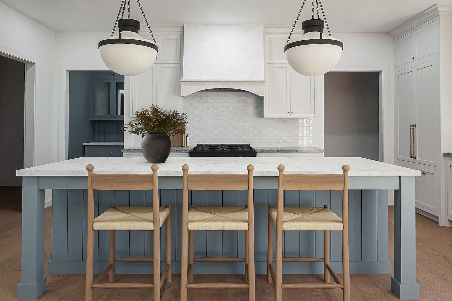 Wooden counterstools in front of a blue island with aged iron pendant lights and stone countertops.