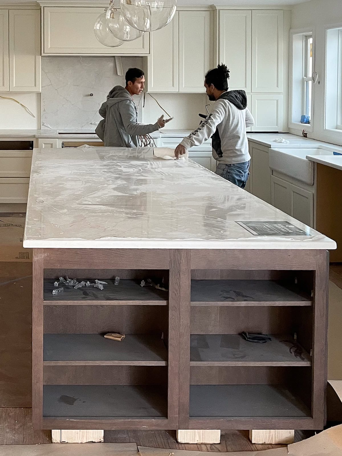 Contractors carefully installing a large marble island countertop in a custom kitchen, illustrating the collaboration required when selecting the right construction partner for a luxury home.