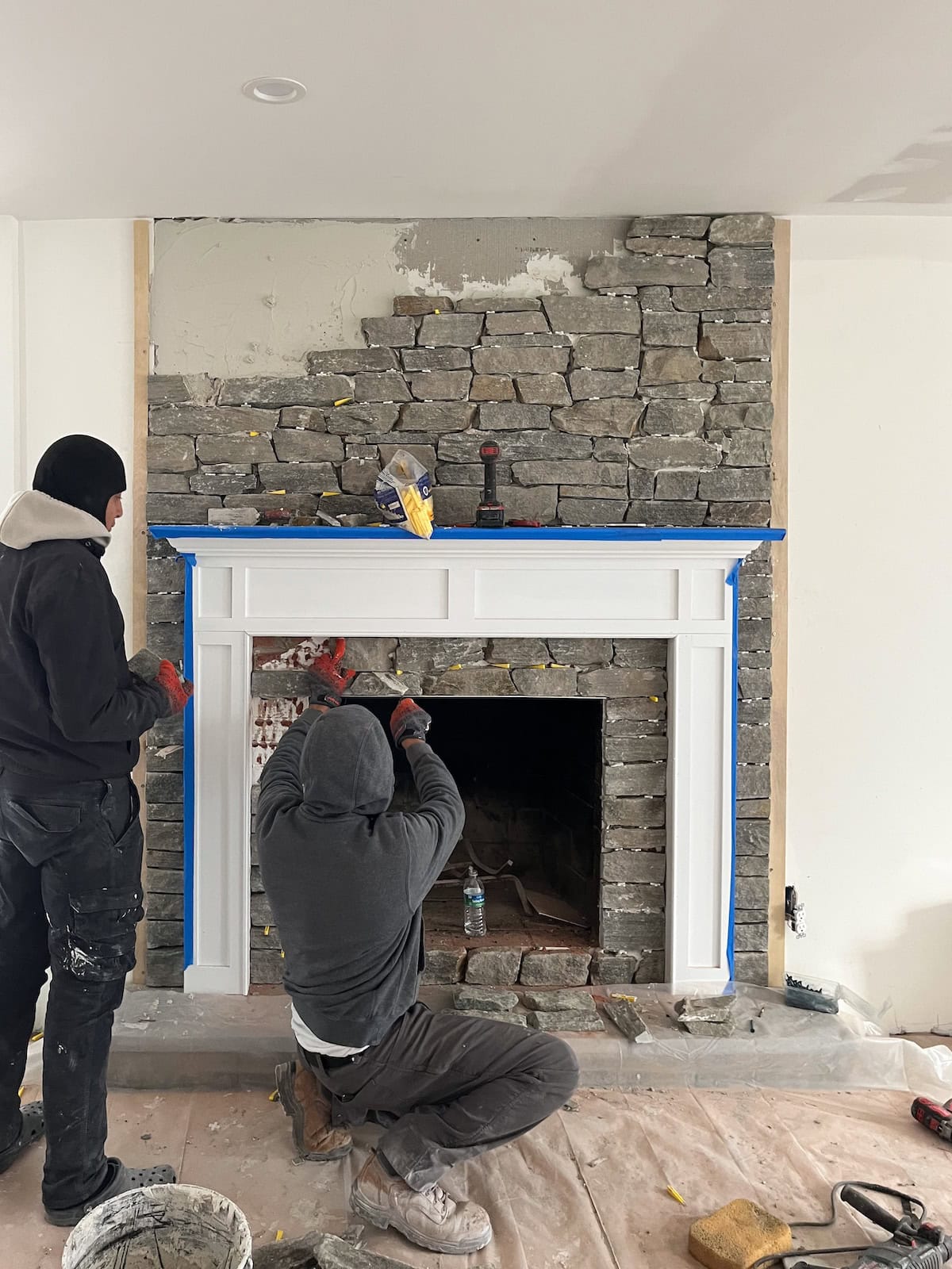 Masons laying a custom stone fireplace surround, demonstrating the high alignment of craftsmanship we prioritize during the residential build process.