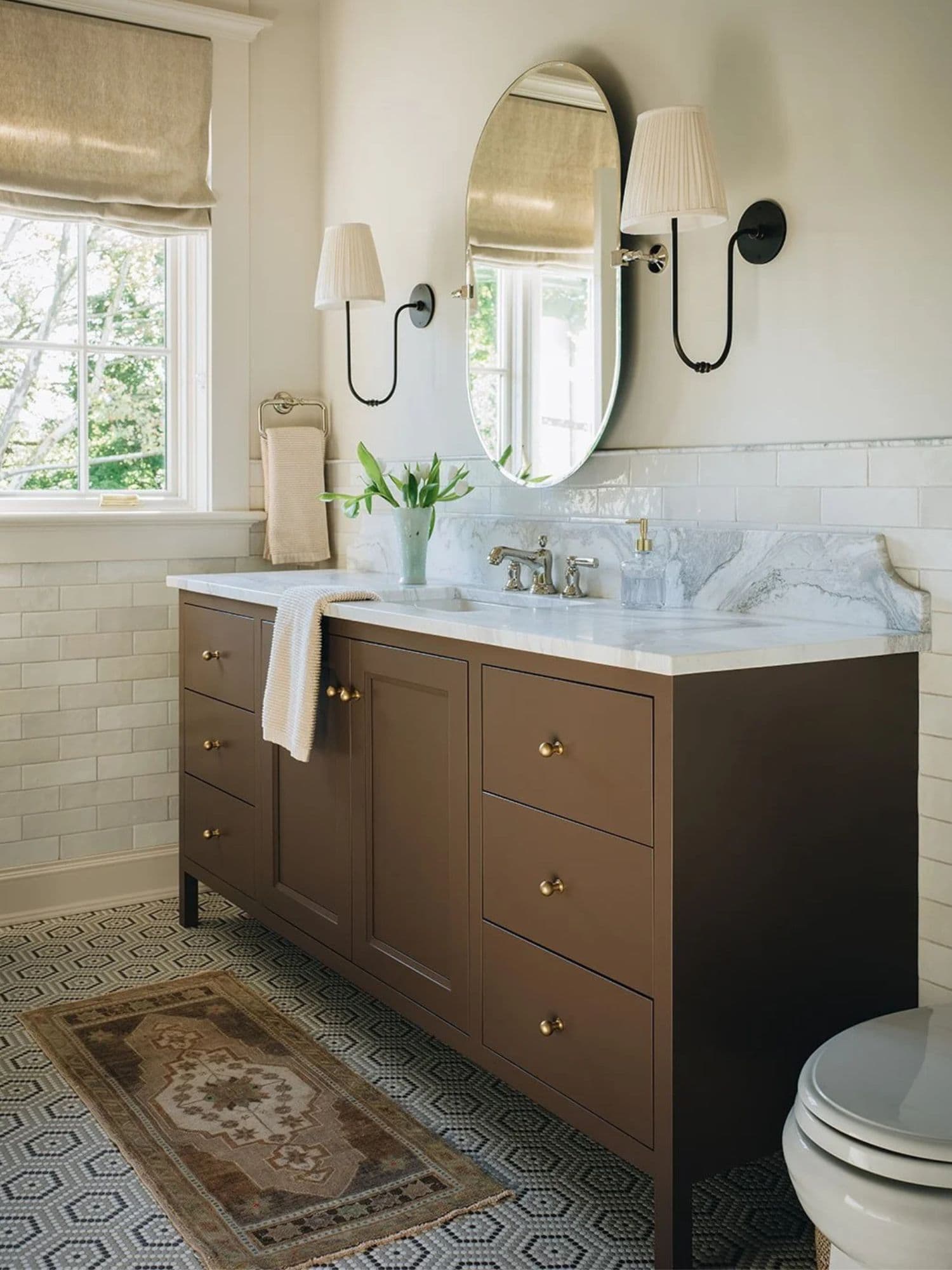 Antique runner rug layered over a patterned tile floor in a bathroom with a marble vanity top.