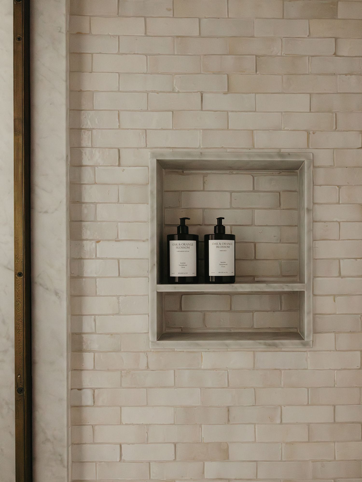 Handmade tile on a shower wall with subtle variations in shape and glaze surrounding a marble framed shower niche.